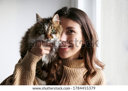 Portrait of young woman holding cute siberian cat with green eyes. Female hugging her cute long hair kitty. Background, copy space, close up. Adorable domestic pet concept. Royalty-Free Stock Photo #1784455379