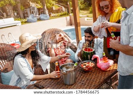 Group of young people having fun at summer vacation and enjoying a poolside party with drinks.