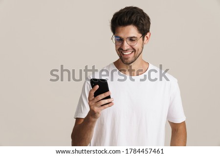 Image of smiling young man in eyeglasses using mobile phone isolated by white background Royalty-Free Stock Photo #1784457461
