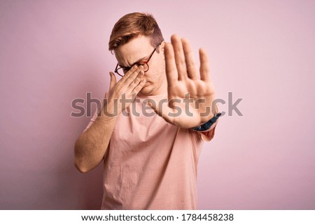 Young handsome redhead man wearing casual t-shirt standing over isolated pink background covering eyes with hands and doing stop gesture with sad and fear expression. Embarrassed and negative concept.
