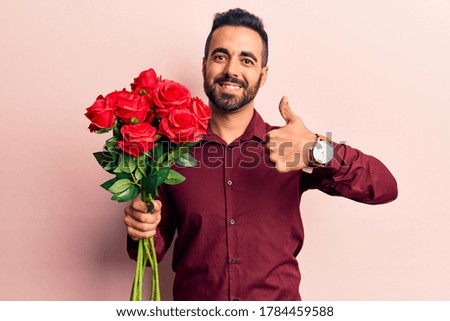 Young hispanic man holding flowers smiling happy and positive, thumb up doing excellent and approval sign 