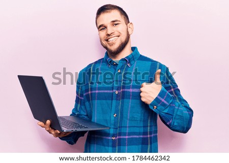 Young handsome man working using laptop smiling happy and positive, thumb up doing excellent and approval sign 