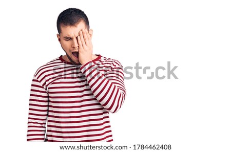 Young handsome man wearing striped sweater yawning tired covering half face, eye and mouth with hand. face hurts in pain. 