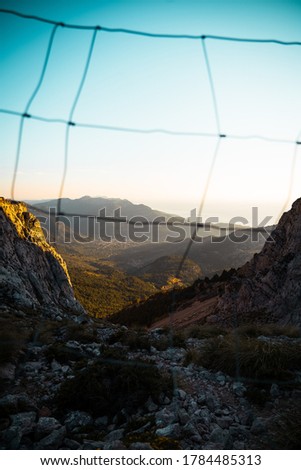 Vertical photo of a view from a mountain of the Valley of Soller (Serra de Tramuntana, Mallorca, Spain) during golden hour and with a fence in front of camera
