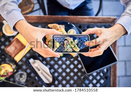 Overhead view of man taking smartphone picture of breakfast in outdoors cafe