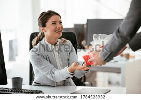 Young businessman giving his colleague present in office. Young man surprise beautiful businesswoman in office.