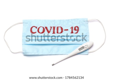 Disposable blue medical face mask with COVID-19 sign and electronic thermometer isolated on white background with clipping path