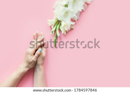 Womans hands with green manicure and white gladiolus flowers on pastel pink background. Top view. Space for text.
