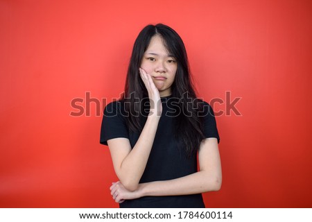 Portrait of Young beautiful asian girl Posing front of camera and using black T-shirt with red isolated background