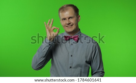 Cheerful glad man showing ok gesture and smiling at camera with optimistic satisfied expression, winking playfully, okay sign of approval. Portrait of guy posing on chroma key background