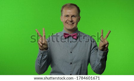 Friendly happy man showing victory sign, hoping for success and win, doing peace gesture and smiling with kind optimistic expression. Portrait of guy posing on chroma key background. People emotions