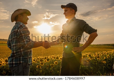 focus on background, Two farmer standing in a wheat field and shake hands on sunset, Agro Business Royalty-Free Stock Photo #1784608997