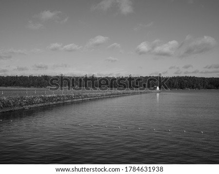 Monochrome photograph showing a pier in Vänersborg, Sweden. It is a stone pier with a white marker at the end. The pier forms a perspective line into the picture.