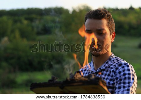 White Caucasian young man or adult guy reading a burning book on blurred forest background.
