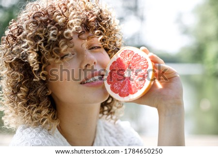 Portrait of a happy healthy woman with curly hair and freckles who holds a grapefruit near her face. Healthy food, health and personal care concept.