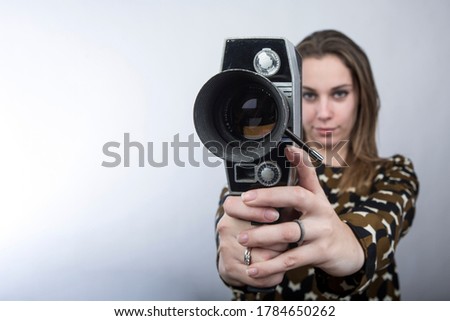 girl with long blonde hair dressed casual has fun playing and making videos with an old movie camera, isolated on white background