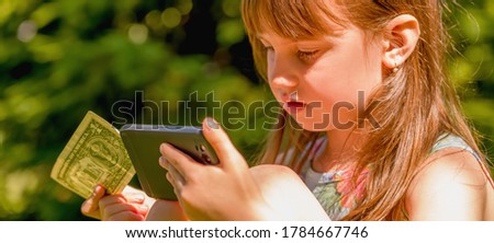 Online banking anywhere and anytime through mobile phones. Portrait of business child girl with smart phone and US Dollar banknote. Humorous picture. Horizontal image.
