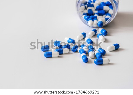 Capsules of the drug, white and blue in color, are scattered from a jar on the table. High-resolution photos. Macro photography with selective focus.