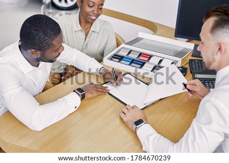 black clients sign a contract while sitting at table with salesman, professional worker of dealership explain terms of the contract and show where to sign