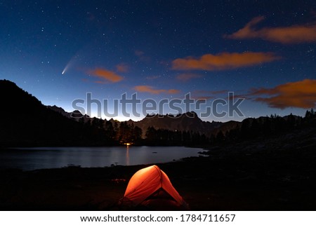 orange tent camping on lake arpy with view of grandes Jorasses with its main summits Pointe Walker and Pointe Whymper in the french alps of Mont Blanc. night view with neowise comet in the starry sky
