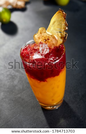 Cuba sling cocktail on dark stone background. Black slate table. Party cocktail with pineapple and berry syrup