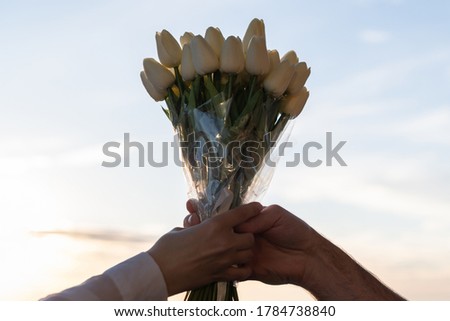 Silhouette of woman and man holding in their hands a bouquet of white tulips flowers against sunset beach.
