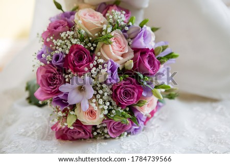 Round beautiful stylish wedding bouquet of purple, pink, cream flowers, white baby wreath and greens, cream wedding dress on the background