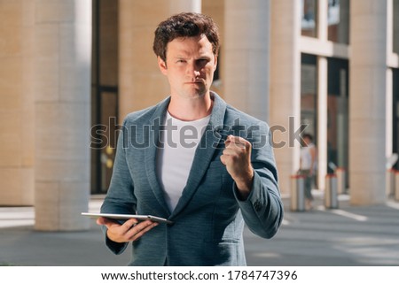 Stylish young man holds a digital tablet against the backdrop of the city background. The concept of a construction engineer with documents near the construction of a multi-storey building