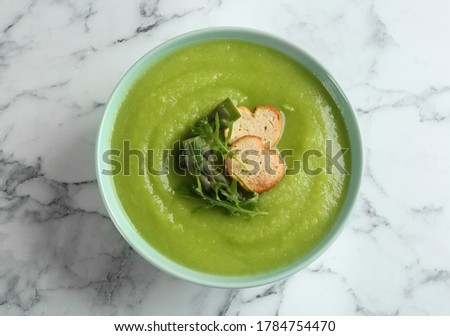 Delicious asparagus soup in bowl on white marble table, top view