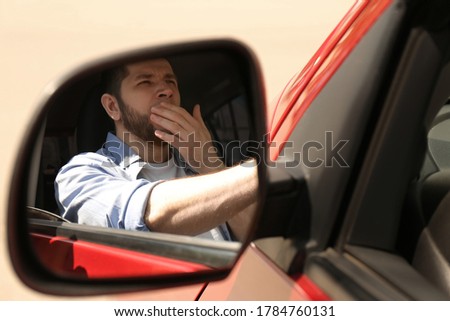 Tired man yawning in his auto, view through car side mirror Royalty-Free Stock Photo #1784760131