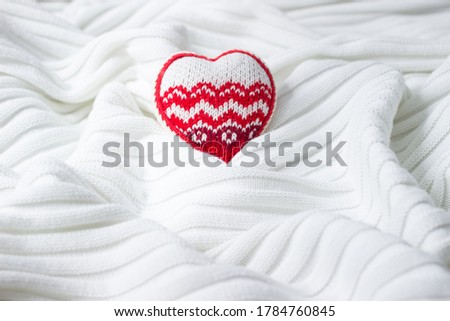Knitted textile background of light color. Heart on a soft white blanket with folds. Knitted cotton.