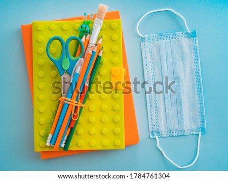 school supplies with medical face mask blue background. Protection schoolchildren students covid-19 coronavirus, school education context pandemic. Flat layer, top view, layout, template, free space