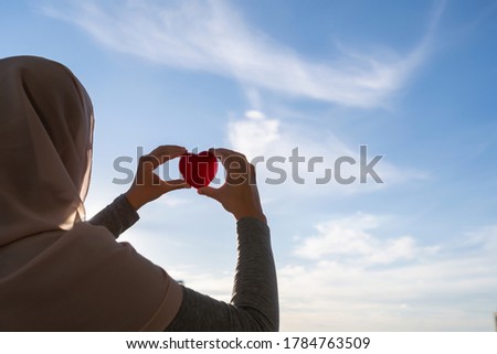 Silhouette of muslim woman in head scarf with red heart on blue sunset sky background. Concept 