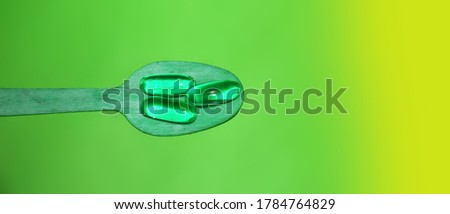 Green Neon Glow Gel Pills on wooden spoon. Addiction or healthcare concept.