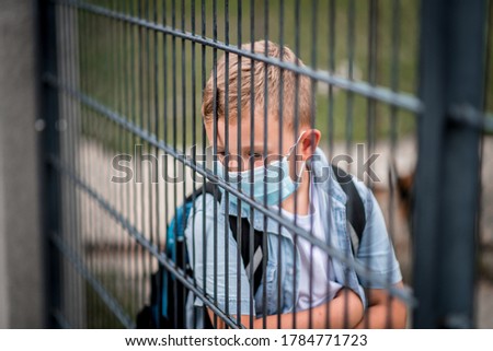 School boy with protective face mask is looking through a wire gate. Back to school.