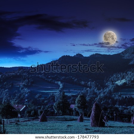 Stack of hay on a green meadow in the mountains in the morning under a blue summer sky at night in moon light