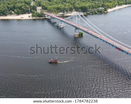 Aerial drone view. A pirate motor boat sails under bridge along the Dnieper River in Kiev.