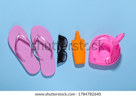 Beach vacation. Inflatable flamingo, flip flops and sunblock bottle, sunglasses on bright blue background. Top view. Minimalism