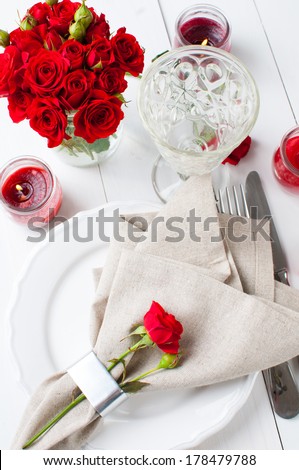 Festive table setting with red roses and candles on white wooden table, rustic style