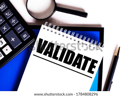 The word VALIDATE is written in a white notebook on a white and blue background next to a calculator, magnifying glass and pen. Business concept