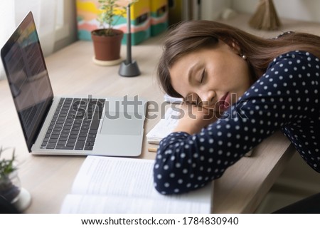 Tired millennial female student fall asleep on desk studying preparing for exam or test, exhausted young woman take nap daydream on notebook, sit at table, feel fatigue, exhaustion, overwork concept Royalty-Free Stock Photo #1784830940
