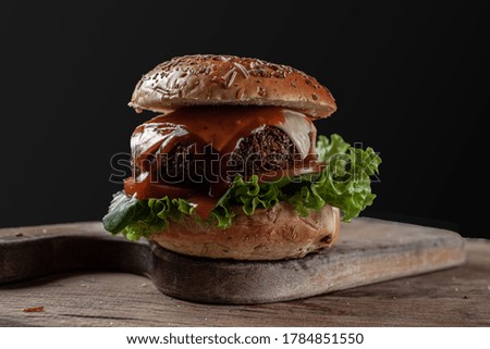Vegetarian hamburger with lettuce and tomato salad. Wooden table and black background.