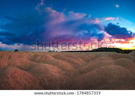 An unusual natural landscape. The landscape is similar to the planet Mars. Sand hills on the background of the colorful sky. Sand, trees, and clouds.