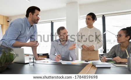 Multiracial businesspeople gather at office meeting engaged in team group discussion together, diverse multiethnic employees talk brainstorm consider company paperwork documents at briefing Royalty-Free Stock Photo #1784859698