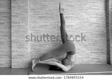 White slim beautiful woman practicing Pilates on the mat at home, graceful movements during a Pilates class. Black and white picture.