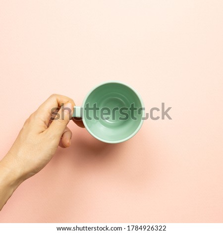 Female hand holding green empty mug cup on pink background. top view