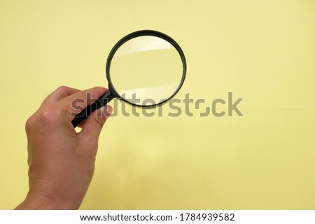 Woman hand holding magnifying glass on yellow background