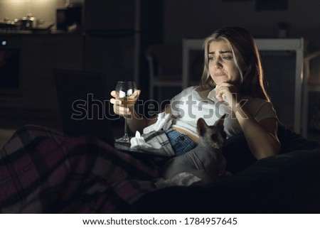 Young beautiful woman watching movie at home at night. A glass of white wine. Online cinema.