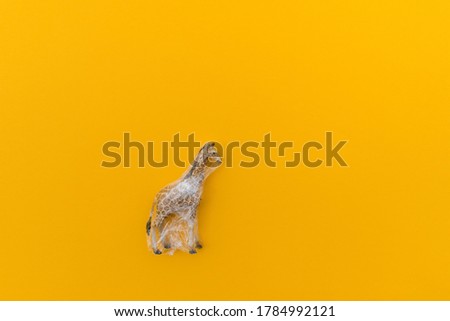 Giraffe is entangled in a plastic bag. Plastic animal concept. Yellow background. Environmental pollution problem.