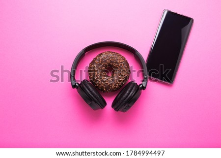 Donut and headphones on a pink background. Concept of business lunch and rest after work.